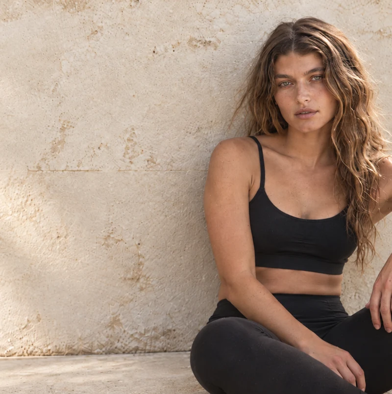 A woman in black athletic wear sitting against a concrete wall